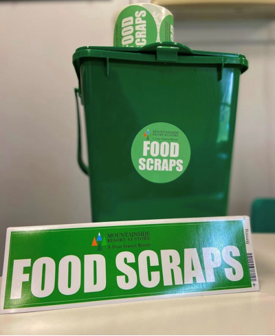A small, green, container with a lid for people to collect food scraps with in their kitchens. Labelled with a sticker that says "Food Scraps."