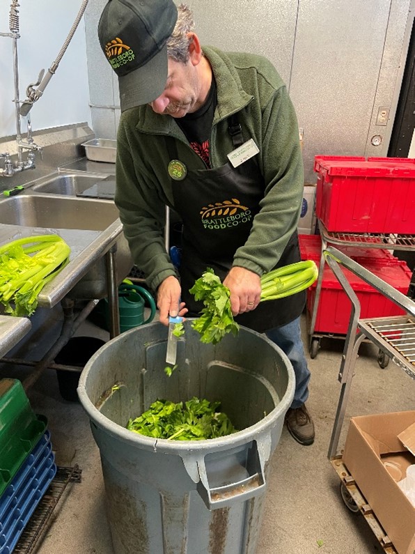 A man chopping the tops off celery into a large food scrap collection container that looks like a standard round garbage can. 